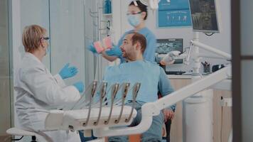 Dentist showing correct way to clean denture with toothbrush, holding artificial jaw for example. Stomatologist giving hygiene lesson to patient learning to brush teeth. Man preventing caries video