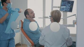 Zahnarzt zeigen Zähne Radiographie zu geduldig auf Dental Stuhl, vorbereiten zum stomatologisch Verfahren mit bohren Werkzeug. Stomatologe halten x Strahl Scan Ergebnisse Vor Prothese Inspektion. video