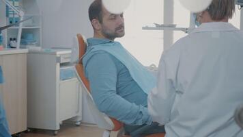 dentiste et patient parlant à propos les dents radiographie analyse à stomatologique examen dans armoire. expert expliquant X rayon diagnostic à adulte dans douleur, en utilisant dentisterie équipement. video