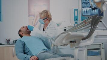 patient med mun öppen tar emot undersökning från tandläkare på oral vård klinik, använder sig av dental instrument. ortodontist hört man med tandvärk för tandvård diagnos. tandläkare arbete video