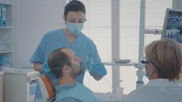 oral cuidado trabajador dando oxígeno máscara con anestésico a paciente. dentista y asistente haciendo anestesia, preparando a realizar dental cirugía en inconsciente hombre a estomatología clínica. video