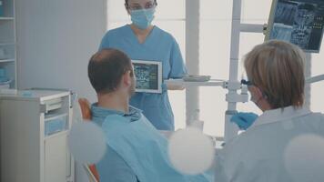 Dentistry assistant holding digital tablet with teeth x ray scan to explain dental procedure to patient. Woman nurse showing radiography diagnosis on screen in stomatology cabinet. video