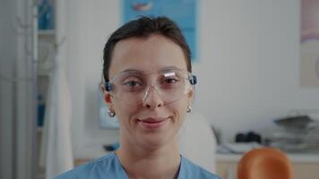 Portrait of assistant with protective glasses at oral care clinic. Stomatology nurse looking at camera and feeling confident about dental practice. Skilled dentistry worker. Close up video