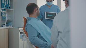 Orthodontic nurse holding x ray results on tablet to show and explain diagnosis to patient in dentistry office. Team of experts showing teeth radiography on device, talking about implant. video