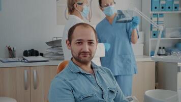 portrait de oral se soucier patient souriant et à la recherche à caméra, séance dans dentisterie armoire. homme ayant vérification rendez-vous avec stomatologue à traiter carie problèmes à dentaire clinique. video