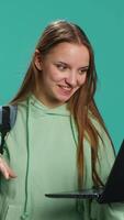 Vertical Smiling woman having friendly conversation with friends during teleconference meeting using laptop, studio background. Girl having fun catching up with mates during online videocall, camera A video