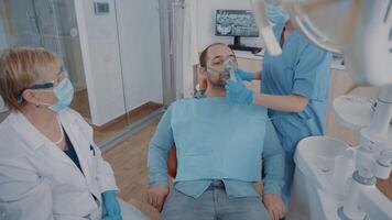 équipe de spécialistes Faire anesthésie sur patient dans dentisterie bureau. infirmière appliquant oxygène masque sur affronter, donnant anesthésique à homme avant début stomatologique procédure dans armoire. video