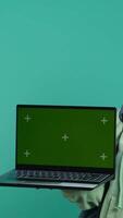 vertikal Lycklig flicka presenter bärbar dator med grön skärm visa, isolerat över studio bakgrund. strålnings tonåring skapande främja annons med attrapp anteckningsbok enhet, kamera en video