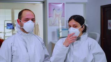 Portrait of team doctor in dental office taking off protective masks looking on camera having marks on face wearing ppe suit in waiting room. Concept of new normal clinic in coronavirus outbreak video