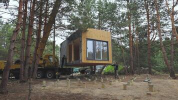 installation av en modern prefabricerad stuga i en skog område under. de bearbeta innebär exakt manövrering och placering av de strukturera till en fundament bland de lång tall träd. video