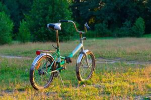 the bicycle stands on a lawn illuminated by the sun against the background of trees photo