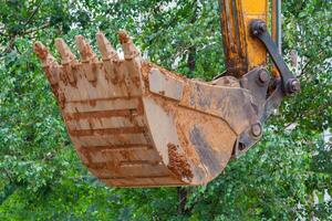 Raised excavator bucket on a background of green trees closeup photo