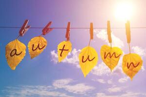 yellow leaves with the inscription - autumn hanging on the clothespin on the background of blue sky and sun photo