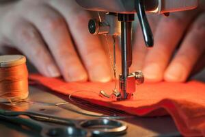 Tailoring process - women's hands behind her sewing, near lies skein of threads and scissors photo