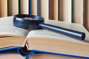 On a open book lies a magnifying glass on a background of book stand in a row photo