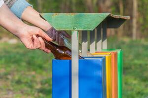 Hand throwing glass bottle in four colors recycling bin in the park photo