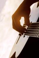 Hand of man playing classic guitar against a background of daylight photo