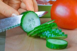 Close-up of female hand slicing fresh cucumbers photo