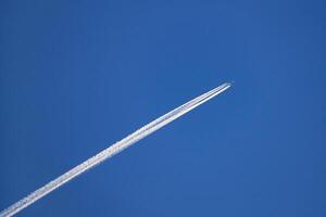 Airplane with an condensation trace behind in the deep blue sky photo