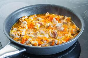 Meat with vegetables is stewed in a frying pan photo