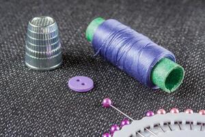 Sewing accessories violet spool of thread, needles, thimble, button on the dark surface photo