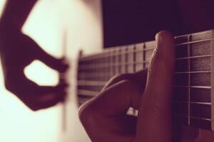 Man's hands playing on classical guitar against a background of white light photo