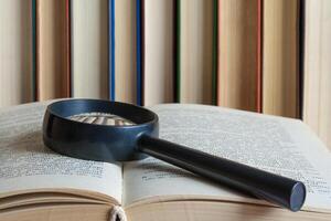 On a open book lies a magnifying glass on a background of book stand in a row search concept photo