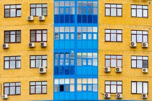 Yellow and blue facade of a modern residential building with air conditioning as background, texture photo