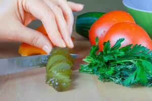 Close-up of female hand slicing salted cucumbers photo