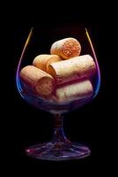 A wine glass filled corks with lighted multi-colored gradient edges on a black background photo