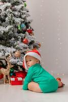 baby in Christmas gnome costume opens gifts near Christmas tree. products for children and holidays photo