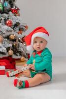 baby in Christmas gnome costume opens gifts near Christmas tree. products for children and holidays photo