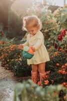 pequeño niña en un amarillo vestir y caucho botas es riego flores en el otoño jardín foto
