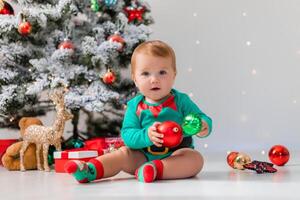 baby in green bodysuit holds colorful Christmas balls in his hands. kid in a Christmas gnome costume photo