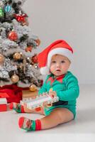 baby in Christmas gnome costume opens gifts near Christmas tree. products for children and holidays photo