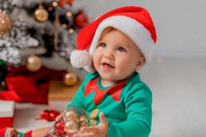 Santa's little helper next to the Christmas tree with Christmas balls in his hands. portrait of baby photo