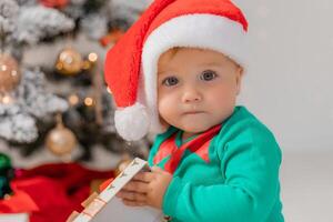 baby in Christmas gnome costume opens gifts near Christmas tree. products for children and holidays photo