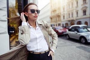 retrato de elegante mujer en Saco en pie en ciudad calle antecedentes y mirando a lado foto