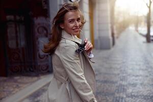 Smiling fashionable woman with sunglasses crossing the city street and looking at camera photo