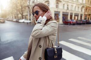 Side view of stylish woman in sunglasses standing on city street background photo