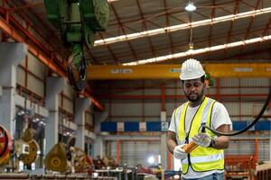 African American engineer worker is using overhead crane hoist to carry raw materials inside metal sheet manufacturing factory for heavy industry photo