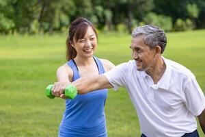 Senior asian man is using dumbbell for weight training strength while his daughter is supporting in the public park for elder longevity exercise and outdoor workout photo