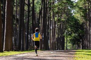 Asian trail runner is running outdoor in the pine forest dirt road with water backpack for exercise activities training to race in the ultra marathon to achieve healthy lifestyle and fitness photo
