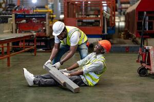 africano americano fábrica trabajador teniendo accidente mientras trabajando en fabricación sitio mientras su colega es Ayudar para la seguridad lugar de trabajo y emergencia foto