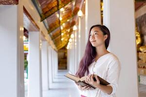Asian buddhist woman is reading Sanskrit ancient Tripitaka book of Lord Buddha dhamma teaching while visiting the temple to chanting and worship inside the monastery photo