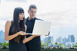 Businessman and businesswoman looking at the report from laptop with skyscraper cityscape view for business and luxury dating photo