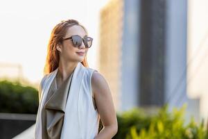 Luxury young Asian CEO woman entrepreneur standing on the rooftop looking to the sun with skyscraper and cityscape on the background with copy space photo