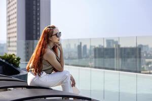 Luxury young Asian CEO woman entrepreneur is sitting by the swimming pool with skyscraper and cityscape on the background for business travel and urban lifestyle concept photo