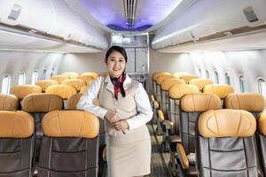 Asian flight attendant posing with smile face at middle of the aisle inside aircraft for welcoming passenger on board with seat on the background photo