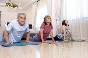 mayor asiático Pareja y hija son haciendo rutina de ejercicio a hogar en cobra yoga actitud con relajante ejercicio para mayor sano y digestión sistema foto